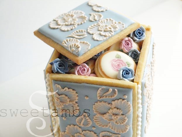 Cookie box with the lid askew, revealing mini cookies and royal icing roses inside.