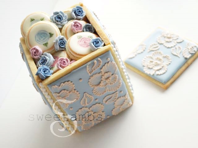 A cookie box decorated with floral brush embroidery and filled with mini cookies and royal icing roses