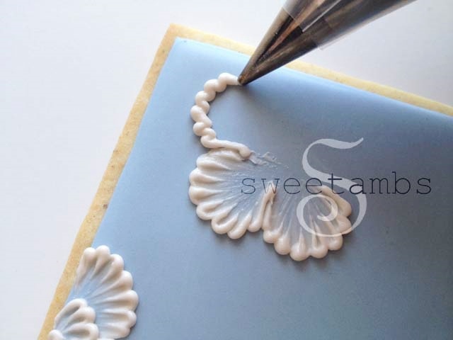 A decorating tip piping a ruffled edge of a flower petal onto an iced cookie.