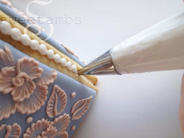 decorating bag filled with white icing and fitted with a tip 5 piping a bead border in the seam of the box.