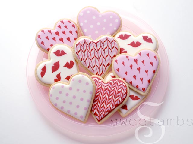 Plate of valentine's day cookies decorated in pink, white, and red royal icing with polka dots, hearts, lips, and herringbone designs.
