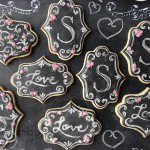 a set of cookies decorated to look like a chalkboard surface. The cookies are decorated with monograms and roses.
