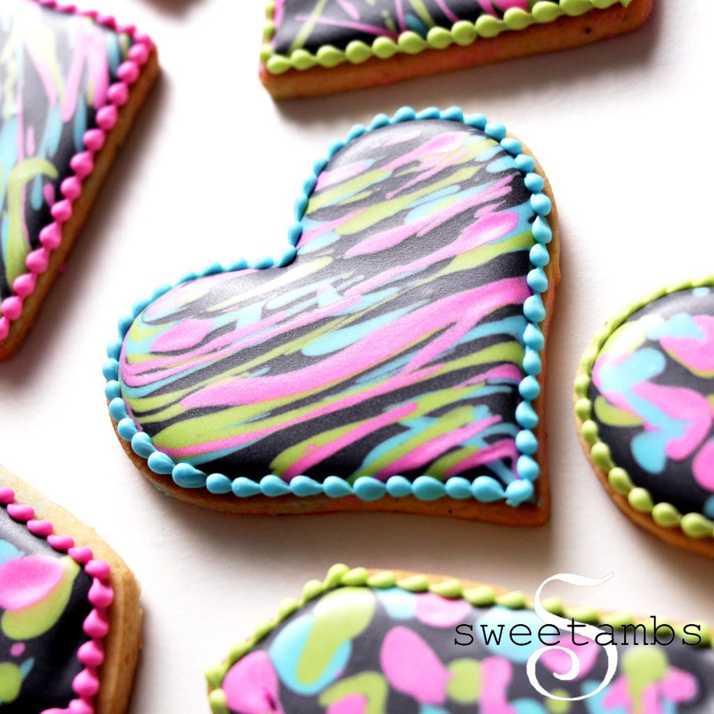 Close up of a heart shaped cookie decorated in black royal icing and splatters of brightly colored royal icing. 