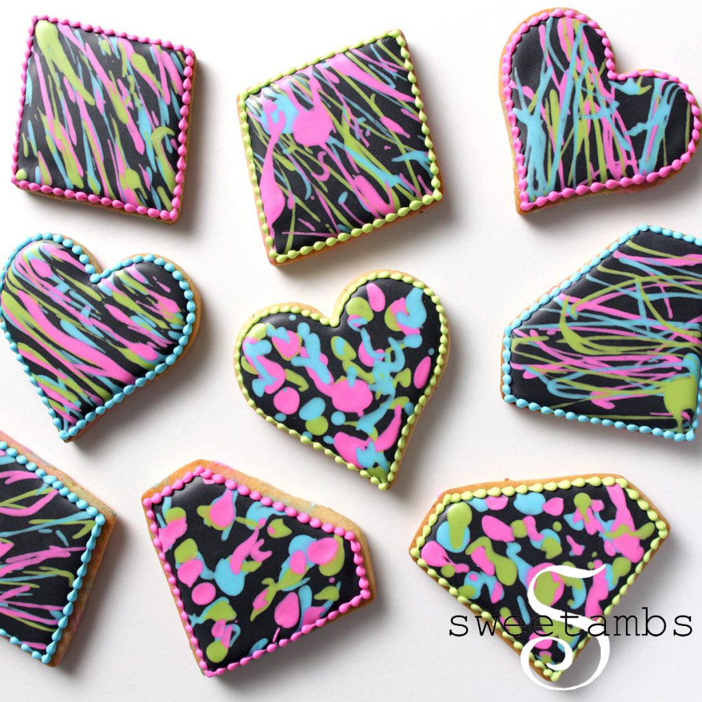 Diamond and heart shaped cookies decorated with black royal icing and splattered with neon pink, blue, and green royal icing