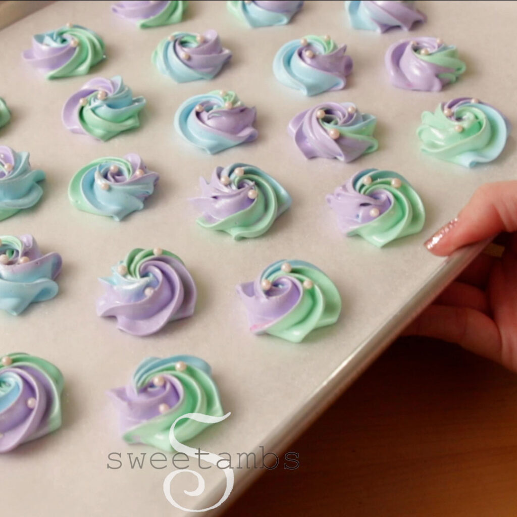 A hand is holding a parchment lined baking sheet full of meringue cookies.