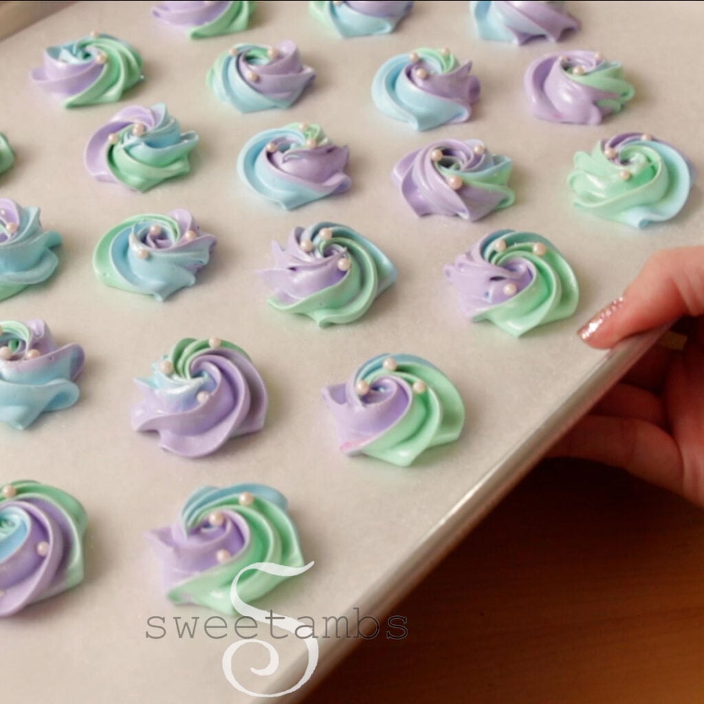 A hand is holding a parchment lined baking sheet full of meringue cookies.