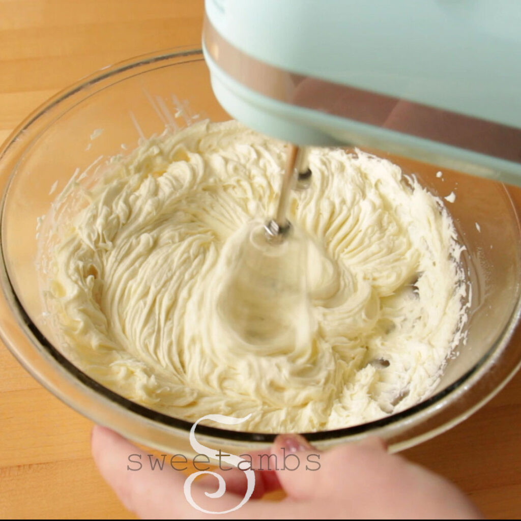 A light blue electric mixer is beating the bowl of white chocolate ganache.
