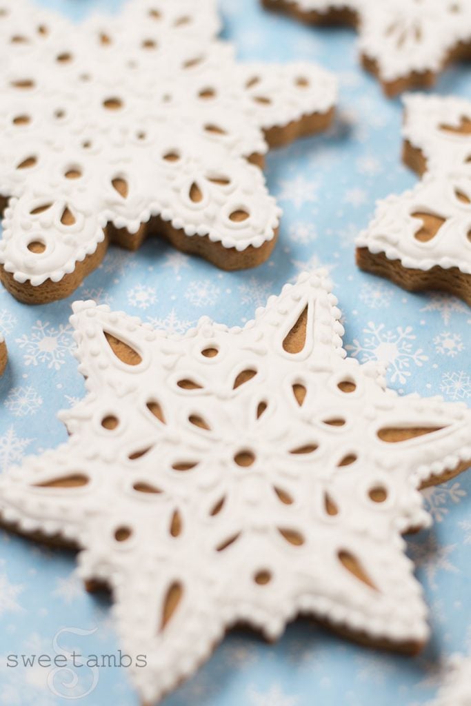 Eyelet lace gingerbread snowflake cookies decorated in royal icing. The cookies are on a light blue background with a snowflake print.