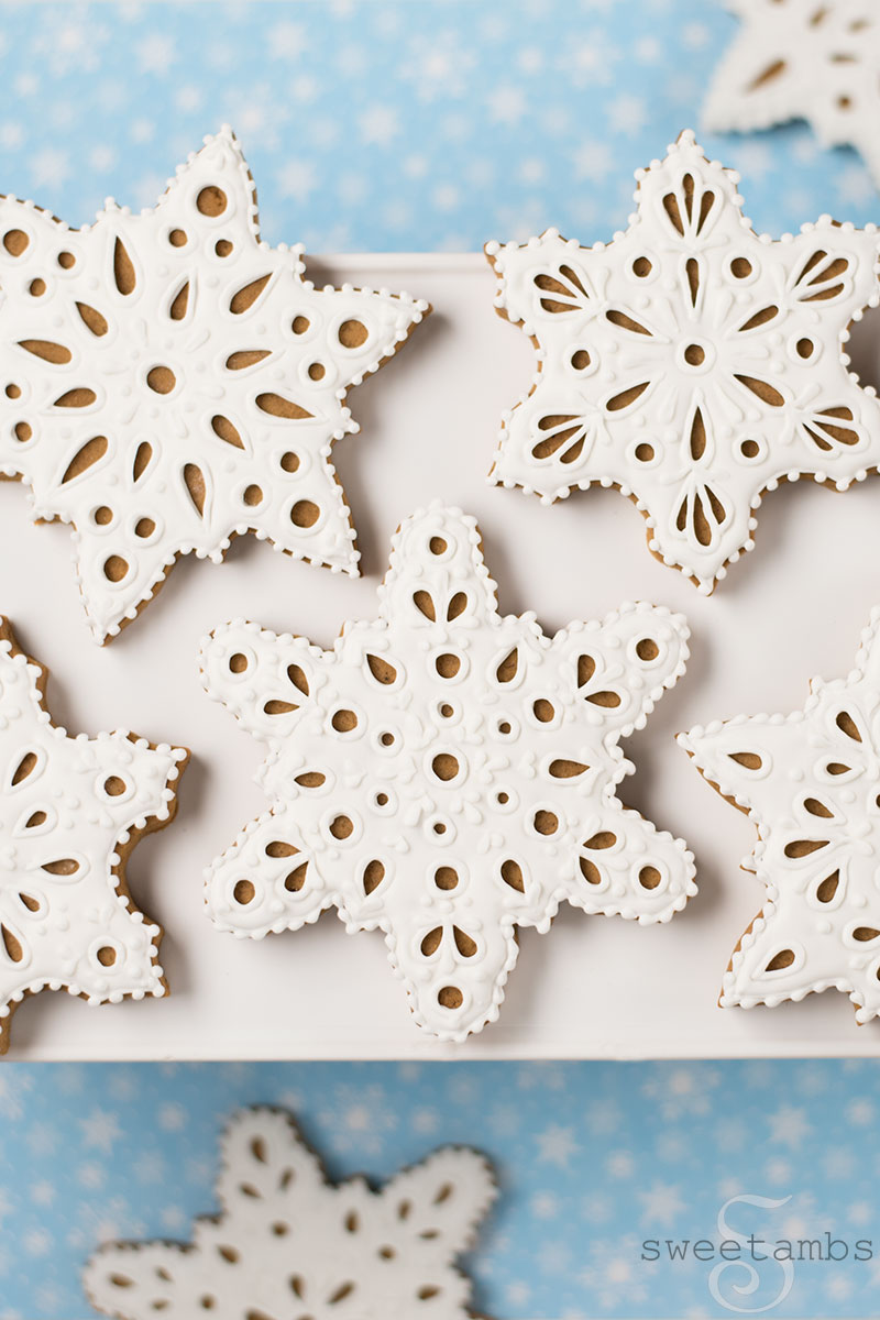 Eyelet lace gingerbread snowflake cookies decorated in royal icing. The cookies are on a light blue background with a snowflake print.