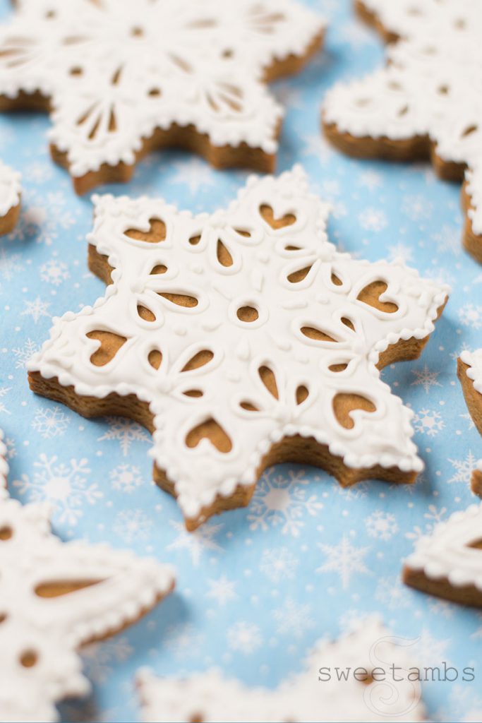 Eyelet lace gingerbread snowflake cookies decorated in royal icing. The cookies are on a light blue background with a snowflake print.