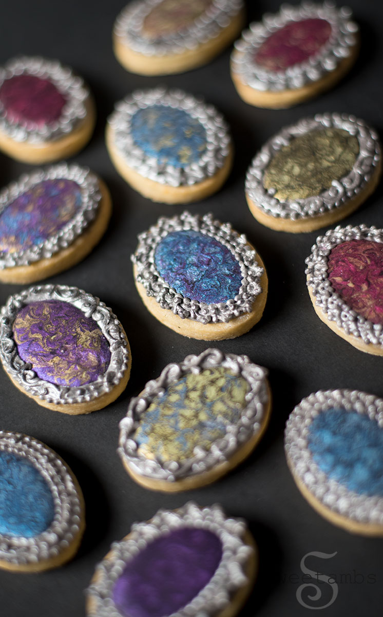 Antique Brooch Cookies. Small oval cookies decorated with pearlized royal icing in jewel tones with intricately piped borders painted with silver edible luster dust.