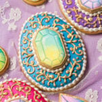 An egg shaped cookie decorated with a jewel cookie, gold filigree, and pearls.