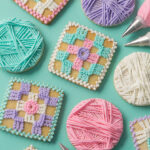 A set of cookies decorated to look like crochet granny squares and balls of yarn. There are decorating bags with  metal tips filled with icing on the edges of the picture. 