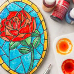 a cookie decorated to look like a stained glass rose. The cookie is surrounded by bottles of food coloring and a palette filled with food coloring.