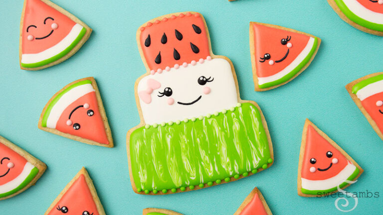 A cookie shaped like a cake and decorated to look like watermelon with a cute face. The cake is surrounded by watermelon slice cookies with cute faces.