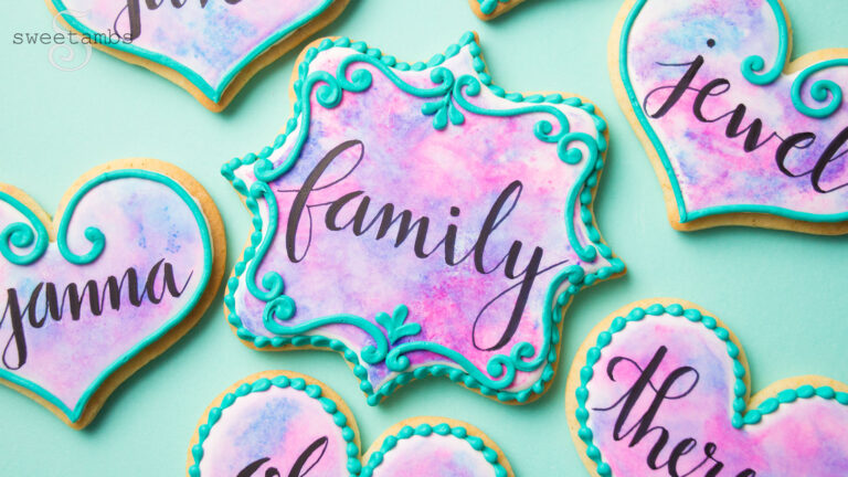 Plaque and heart shaped cookies decorated with a watercolor wash and black calligraphy with piped details around the edges.