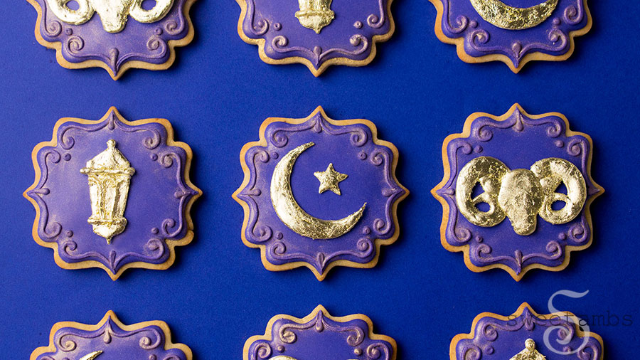 Ornate plaque shaped cookies decorated with deep purple icing. The cookies are adorned with a gold lantern, a gold crescent moon and star, and a gold ram. The edges of the cookie are decorated with a filigree design and gold luster dust.