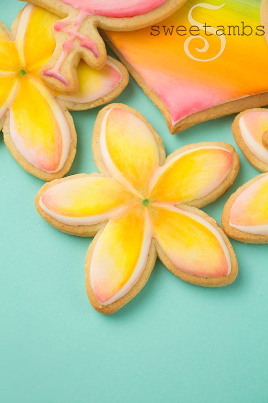 A cookie decorated to look like plumeria. The legs of the flamingo cookie and the bottom of the heart cookie are above the plumeria cookie.
