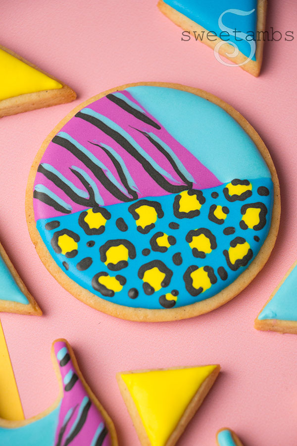 A round cookie decorated with brightly colored animal prints and smaller triangle cookies in solid colors. The cookies are on top of a color block background. 