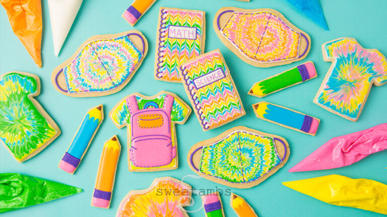 Back to school cookies. This set of cookies is decorated with brightly colored royal icing to look like tie dye t-shirts, a backpack, pencils, spiral notebooks with the words Math and Science written on them, and tie dye masks. There are tipless decorating bags filled with icing around the cookies.