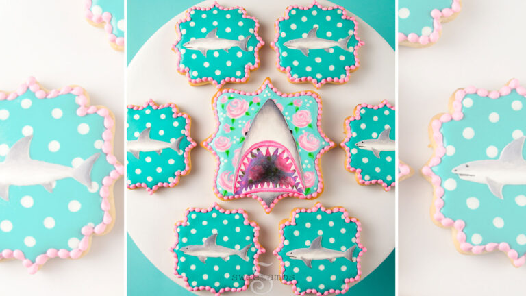 Plaque shaped cookies decorated with roses, polka dots, and sharks. The cookie in the middle is decorated with a shark with an open mouth showing its teeth. The smaller cookies surrounding it are decorated with profiles of small sharks.