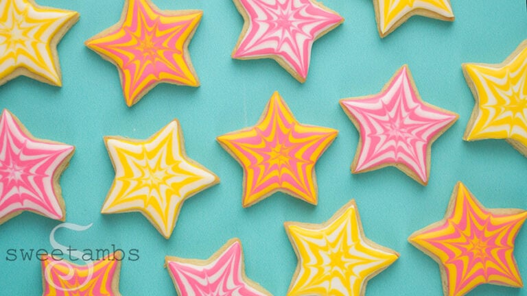 Small star cookies decorated with a starburst design in yellow, pink, and white royal icing.
