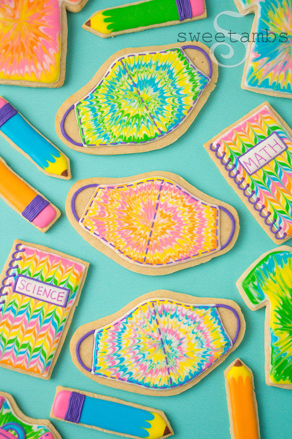 Back to school cookies. This set of cookies is decorated with brightly colored royal icing to look like tie dye t-shirts, a backpack, pencils, spiral notebooks with the words Math and Science written on them, and tie dye masks.