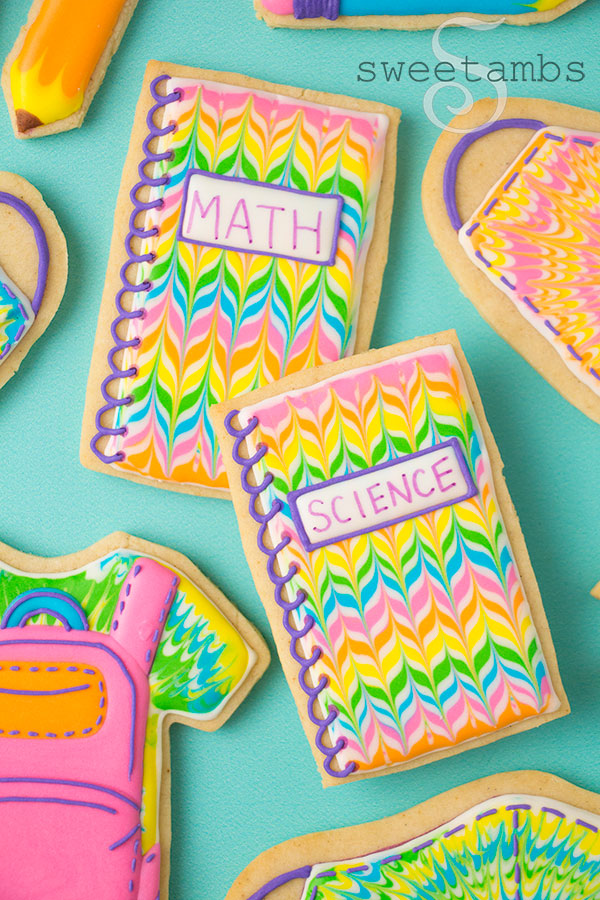 Back to school cookies. This set of cookies is decorated with brightly colored royal icing to look like tie dye t-shirts, a backpack, pencils, spiral notebooks with the words Math and Science written on them, and tie dye masks.