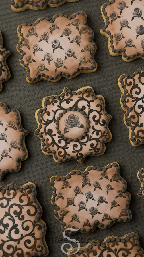 Royal icing roses and filigree cookies for Halloween - a set of square and rectangle plaque shaped cookies decorated with black royal icing roses and filigree on a taupe base. The cookies are dusted with bronze edible luster dust around the edges. The cookies are on a dark gray background.