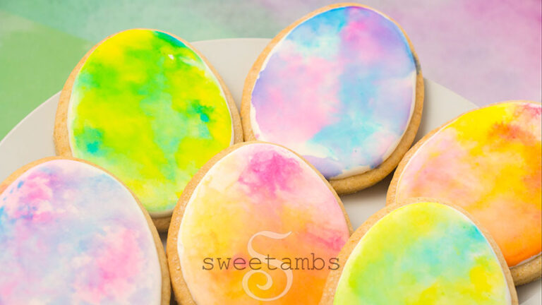 watercolor easter egg cookies - Egg shaped cookies decorated with royal icing and watercolor in pastel colors. The cookies are on a white plate over a watercolor paper background.