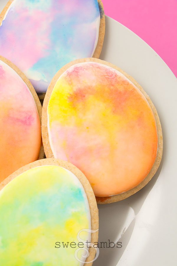watercolor easter egg cookies - Egg shaped cookies decorated with royal icing and watercolor in pastel colors. The cookies are on a white plate on a pink background.