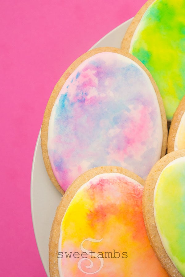 watercolor easter egg cookies - Egg shaped cookies decorated with royal icing and watercolor in pastel colors. The cookies are on a white plate on a pink background.