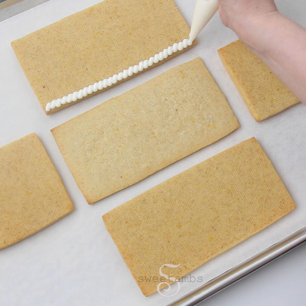 A hand piping icing to the bottom edge of one of the sides of the cookie box.