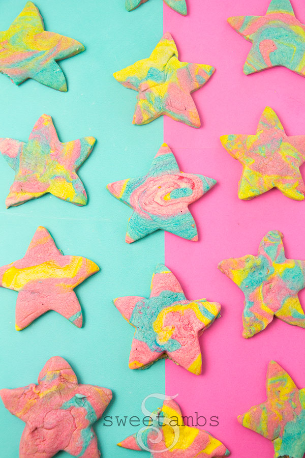 Star cookies with colorful swirl patterns are on a teal and pink background