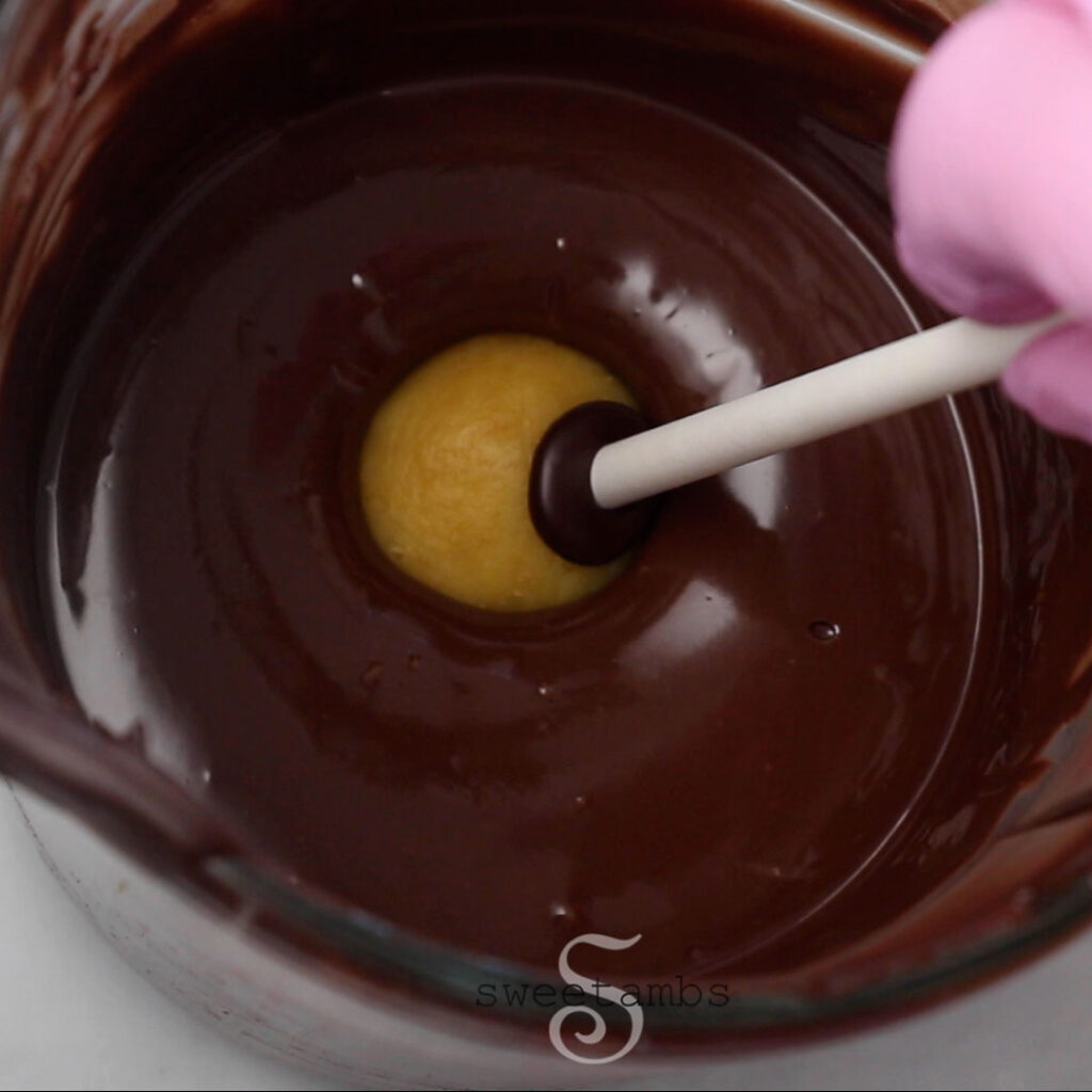 A cake popped being dipped into melted chocolate.