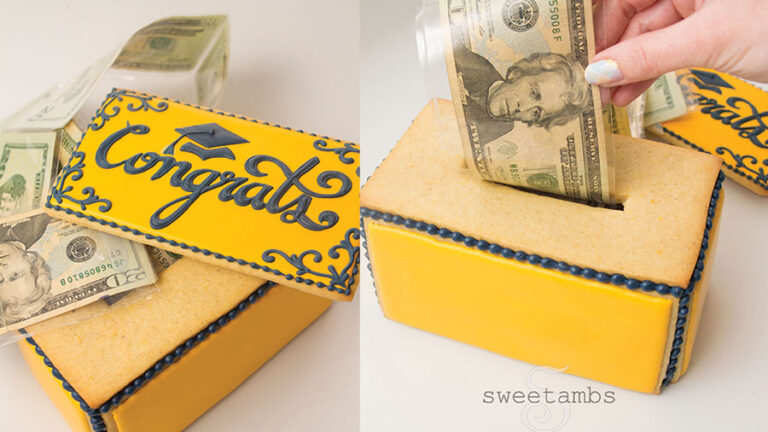 The left side of the frame shows a cookie box with money coming out of it. The top of the box is decorated in royal icing with the word "congrats" and a graduation cap. The right side of the frame shows a hand pulling a $20 bill out of the box. The nail on the thumb is painted with a pastel plaid design.