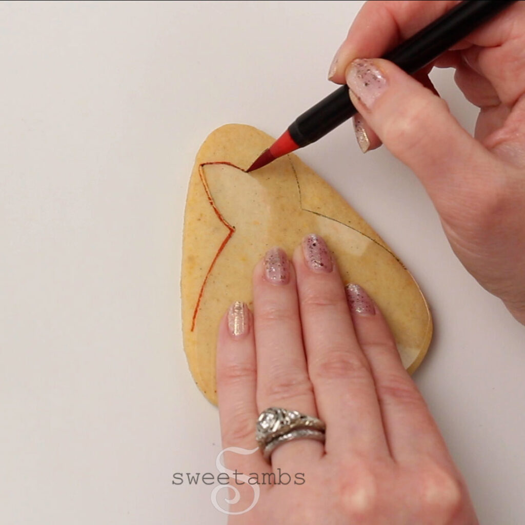 Een doorzichtige sjabloon in de vorm van een jurk overtrekken op een koekje in de vorm van een snoepgraan met een eetbare inktmarker