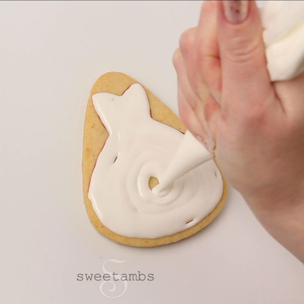 Een tiploze spuitzak die witte royal icing in de vorm van een jurk aanbrengt op een koekje in de vorm van een snoepgraan 