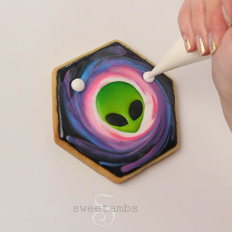 A piping bag filled with white royal icing is piping dots on the cookie