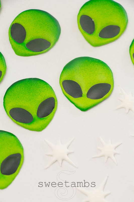 A group of bright green alien face royal icing transfers and white star royal icing transfers