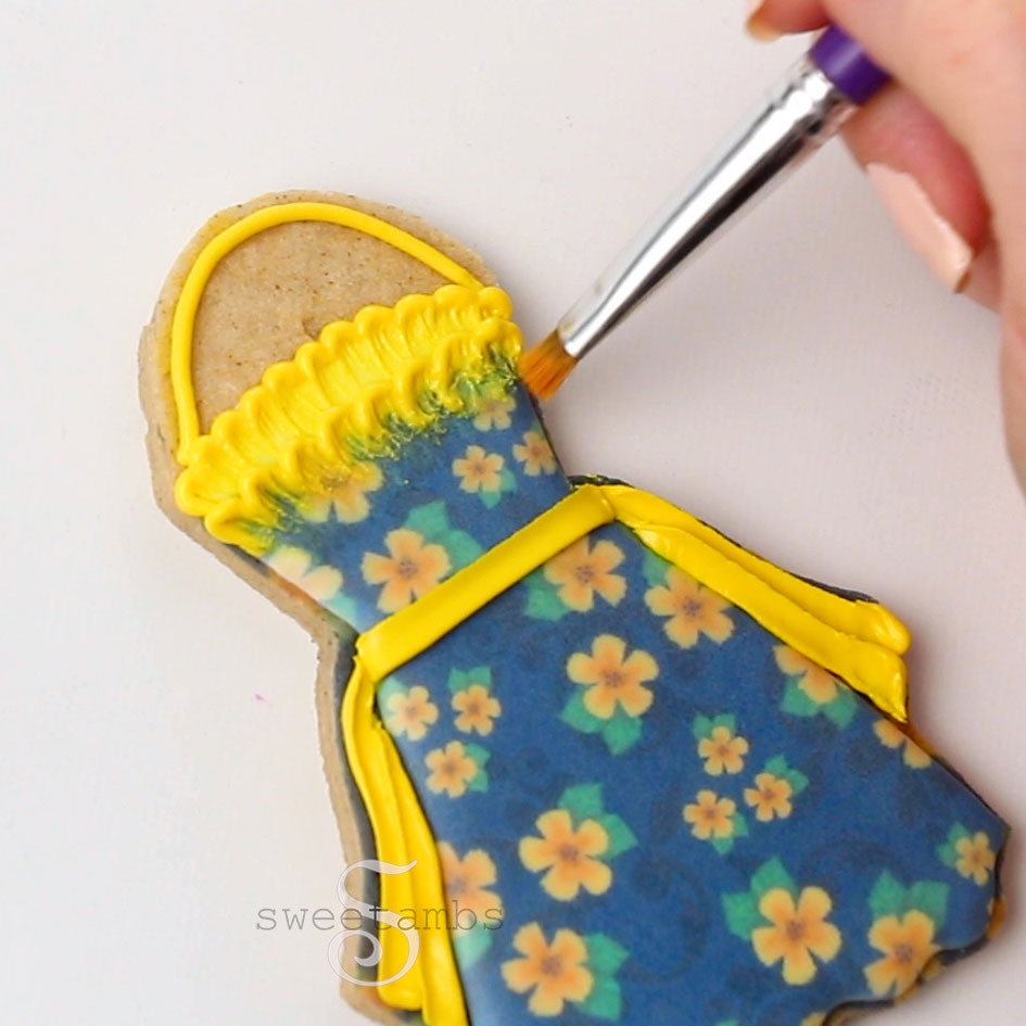 Brushing the icing on the apron cookie to create lace trim with the brush embroidery technique