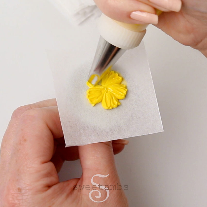 Piping a yellow flower on a parchment lined flower nail with a petal tip 59s