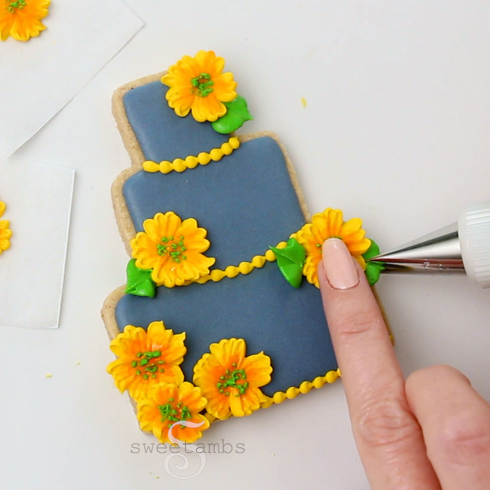 Piping leaves on the flowers on the tiered cake cookie