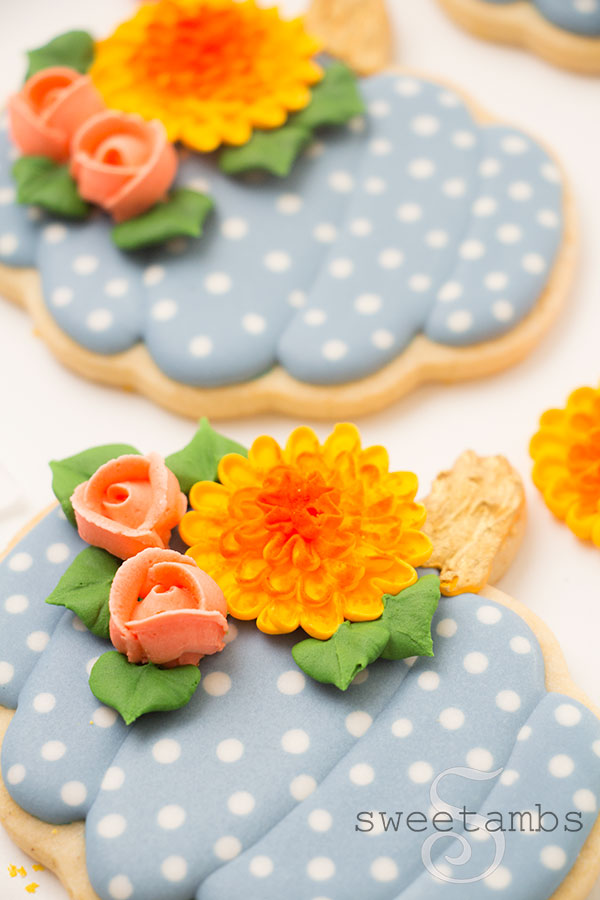 A close up of the pumpkin cookies decorated with light blue royal icing and white polka dots with roses and chrysanthemums.