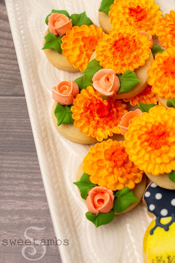A close up of royal icing chrysanthemums and roses on the fall mason jar cookie. The cookies are on a platter with a cable knit design on a wooden background