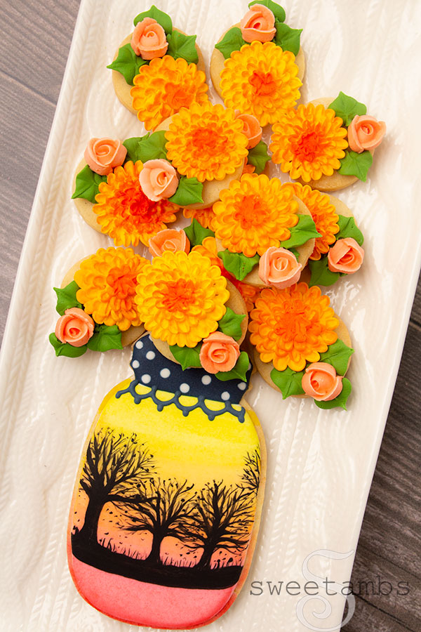 fall mason jar cookie on a platter. The cookie is decorated with a fall sunset scene and filled with royal icing chrysanthemums and roses.