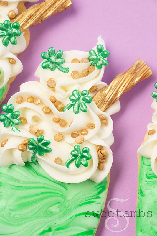 A close up of cookies decorated to look like Shamrock Shakes with homemade royal icing sprinkles and gold candy straws