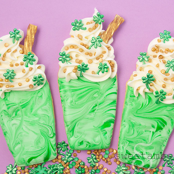 3 cookies decorated to look like Shamrock Shakes with homemade royal icing sprinkles and gold candy straws