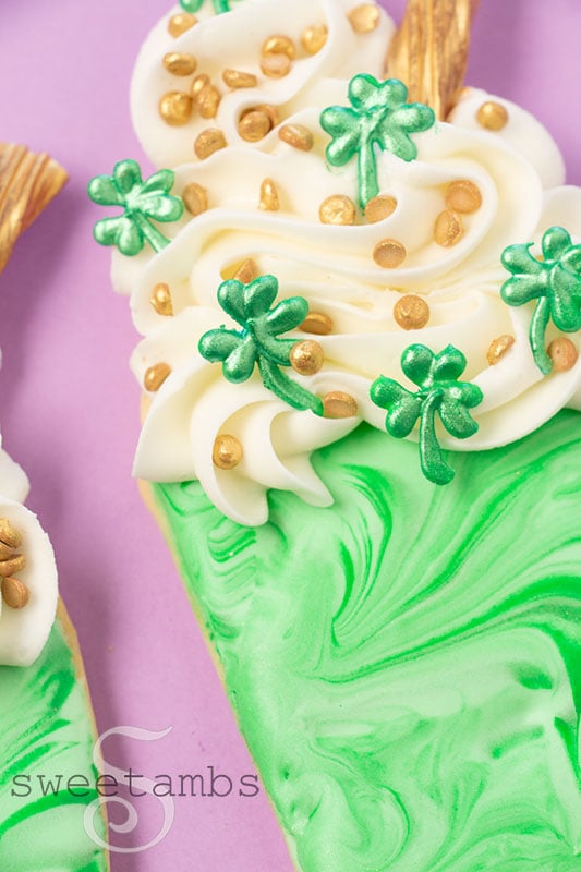 A close up of cookies decorated to look like Shamrock Shakes with homemade royal icing sprinkles and gold candy straws