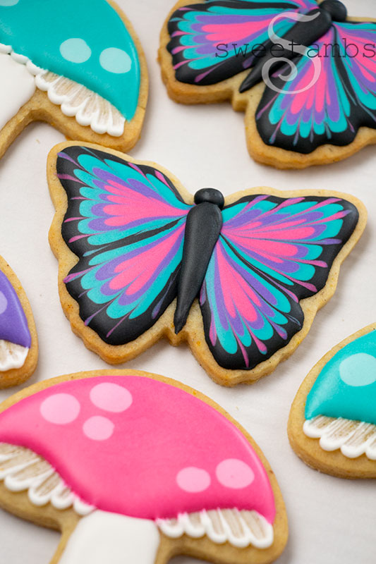 A decorated butterfly cookie surrounded by decorated mushroom cookies